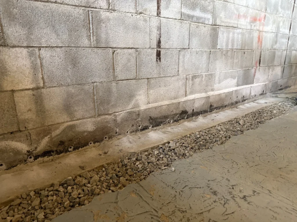 Interior basement waterproofing system installation with weep holes, drainage stone, and moisture control improvements in Patterson, NY.